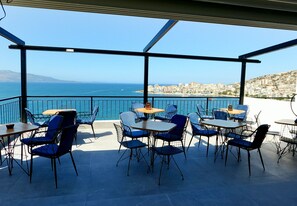 An outdoor terrace with tables and chairs, overlooking a coastal cityscape. - Afrodite Suites (Sarandë)
