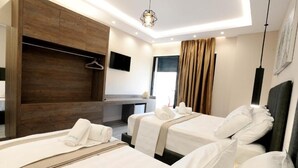 A hotel room with two beds, a wooden wardrobe, a flat-screen TV, and a large window with curtains. - Afrodite Suites (Sarandë)