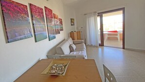 Una sala de estar con un sofá, una mesa de comedor con una bandeja de guijarros, y vistas a un área exterior con una mesa y sillas a través de un ventanal.