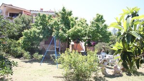 Un barrio residencial con una casa de piedra, un columpio azul y varios arbustos verdes.