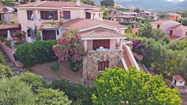 Una villa de estilo mediterráneo con una escalera de piedra, abundante vegetación y techos de tejas rojas.