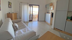 Una sala de estar con un sofá, una mesa de madera y una zona de cocina con armarios y un refrigerador.