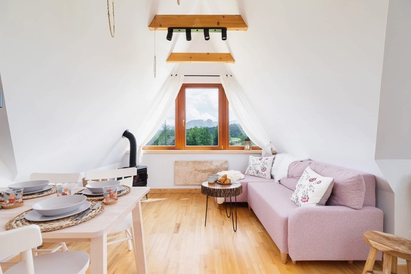 A cozy living area in an attic featuring wooden floors, a comfortable pink sofa, and large windows for natural light.
