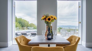 Un tavolo da pranzo con un vaso di girasoli e bottiglie di vino, sedie gialle e vista sull'esterno.