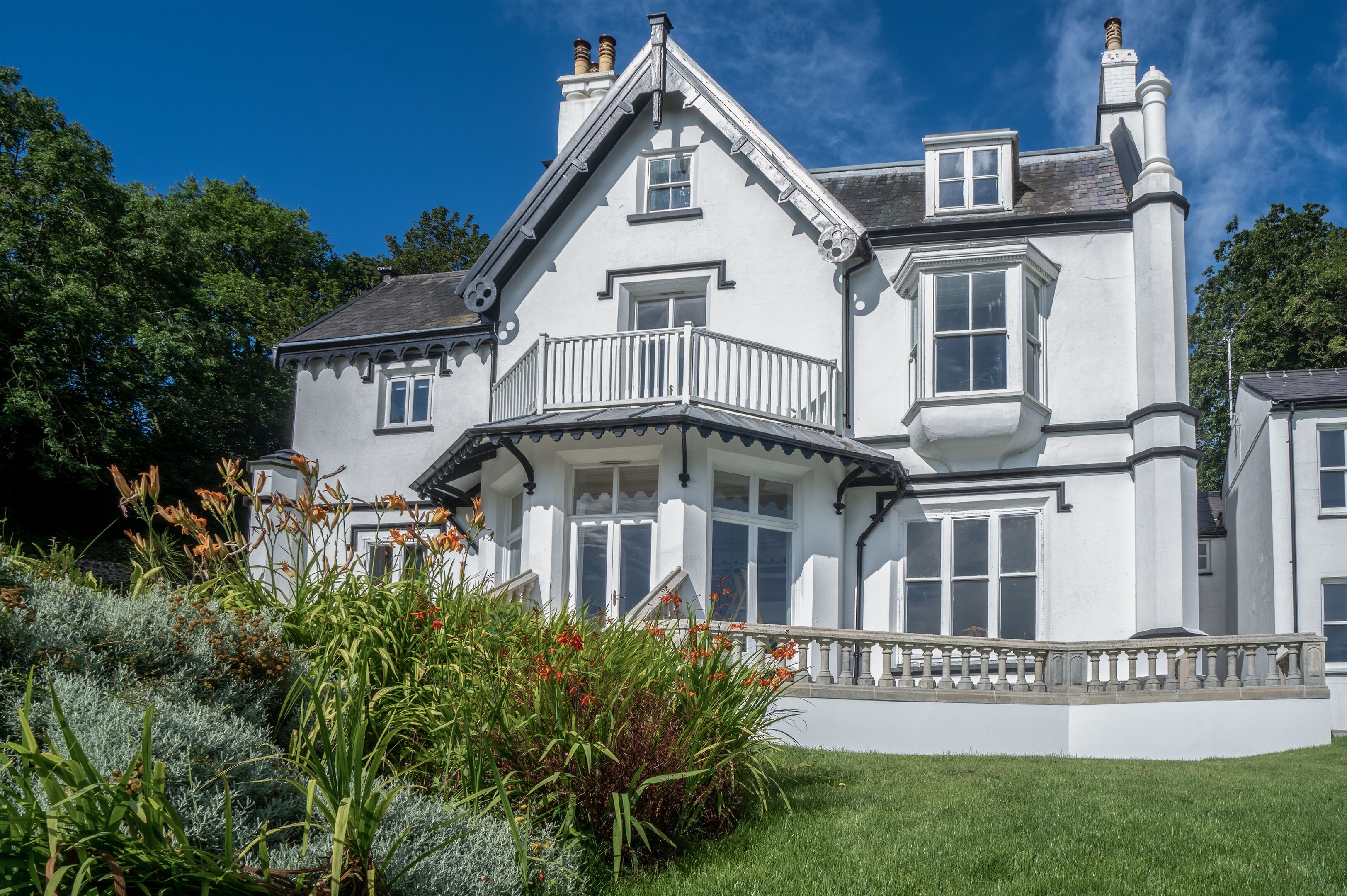 A large, white, two-story house with a balcony and a well-maintained garden.