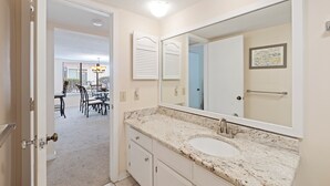 A bathroom with a large mirror, a sink, and a door leading to a dining area.