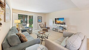 A living room with a sofa, armchairs, a coffee table, a TV, and a bookshelf.