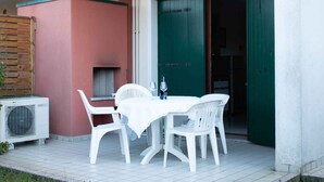 Un patio con tavolo e sedie bianche, un piccolo barbecue e una porta verde.