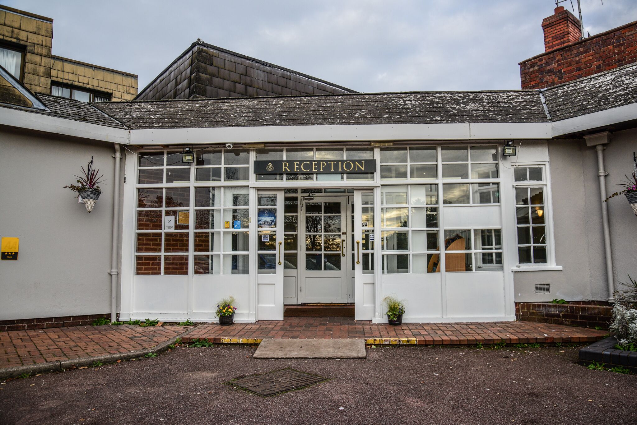 A reception area with a sign above the door, a brick entrance, and potted plants on either side.