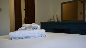 A neatly made bed with folded towels, a dresser with drawers, and a mirror on the wall.