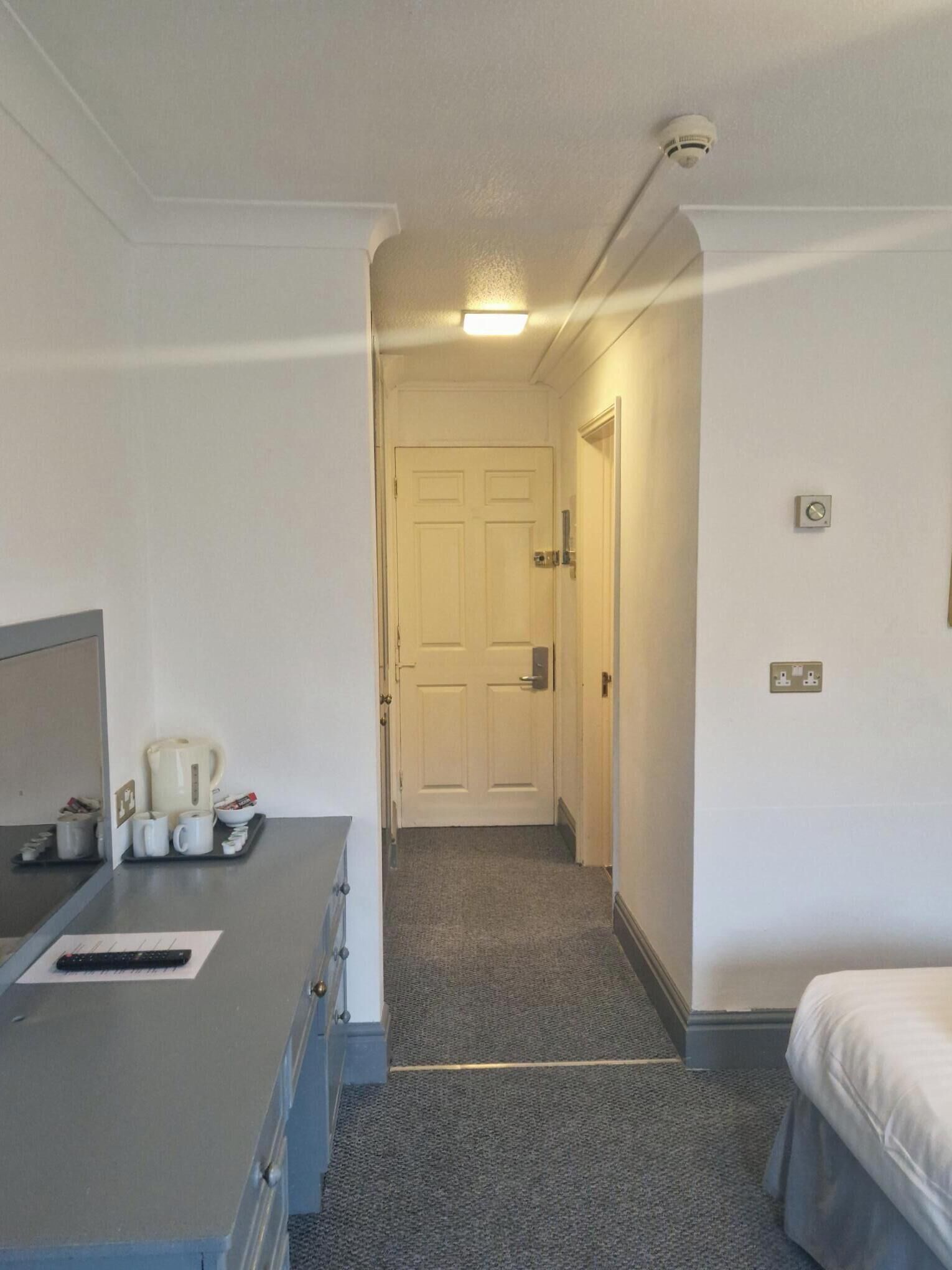 A hotel room with a desk, a bed, a coffee maker, and a door leading to another room.