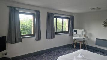 A hotel room with a bed, a desk, a chair, and two windows with curtains.
