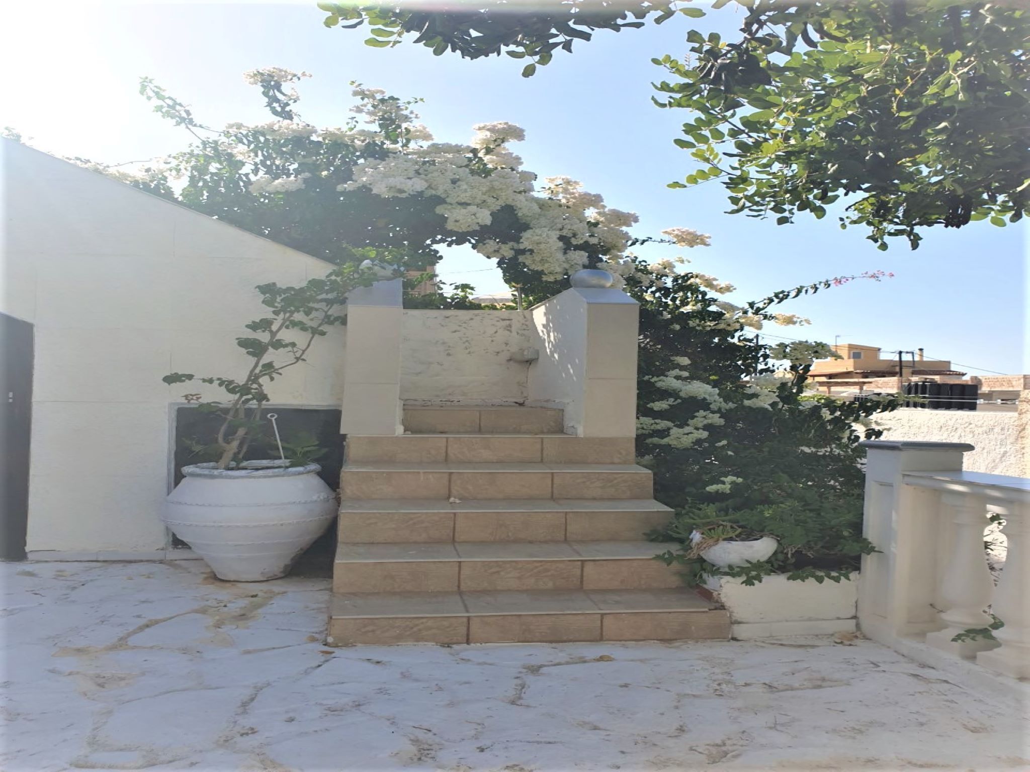A staircase leading up to a white wall with a white pot on the left and a white railing on the right.