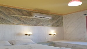 Ett hotellrum med två sängar, en vägg med marmorliknande mönster, en luftkonditioneringsanläggning och två vägglampor.