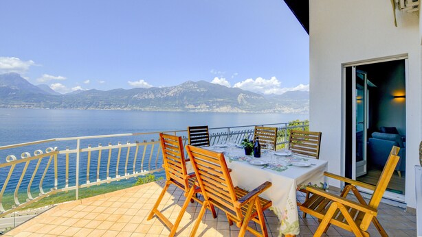 A terrace with a table set for two, overlooking a body of water and mountains. - Casa Bellavista Brenzone (Brenzone)