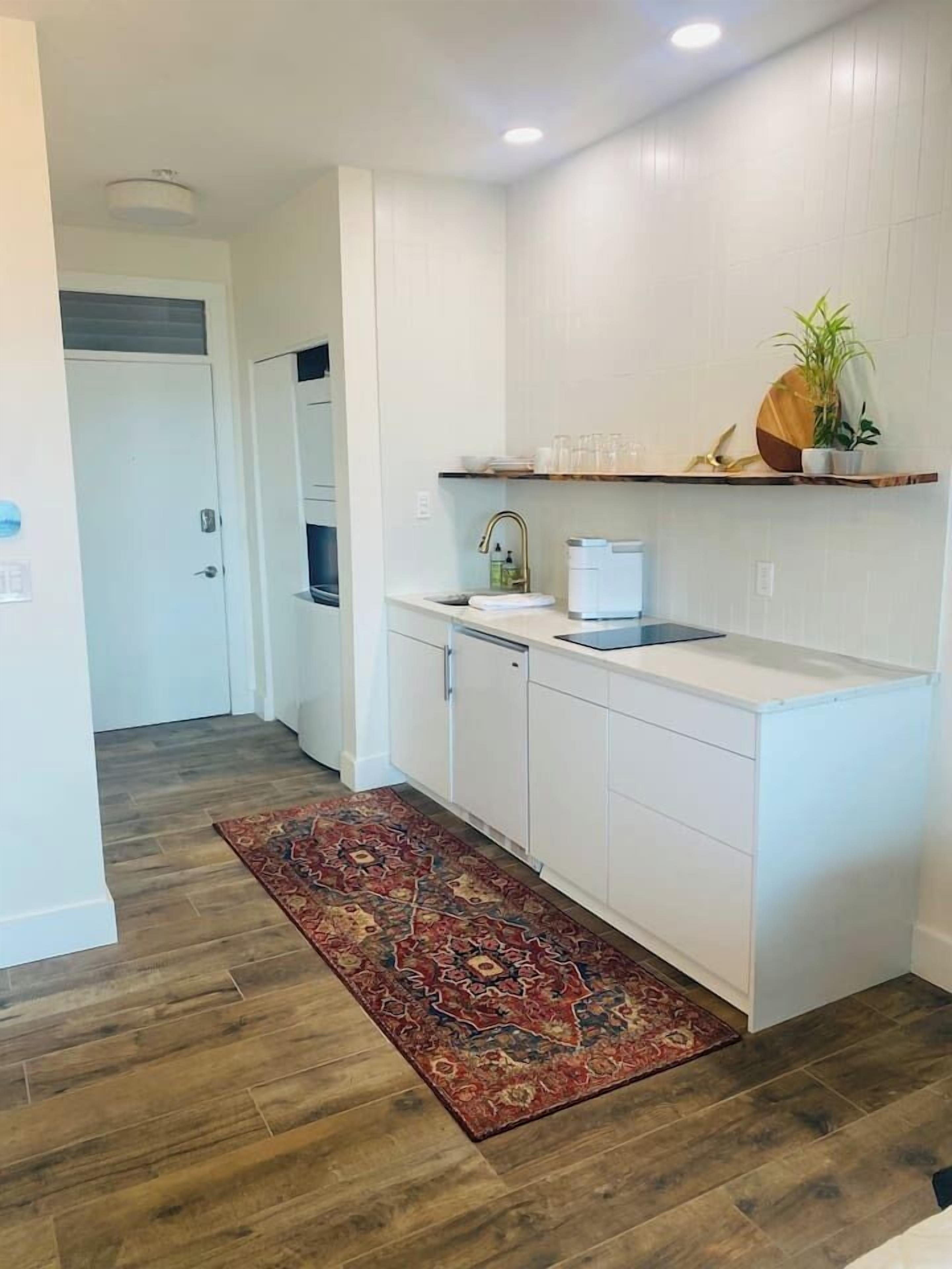 Une cuisine moderne avec des meubles blancs, un plancher en bois et un tapis décoratif.