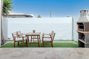 Un patio con suelo de baldosas hexagonales, una mesa de madera con sillas y una parrilla.