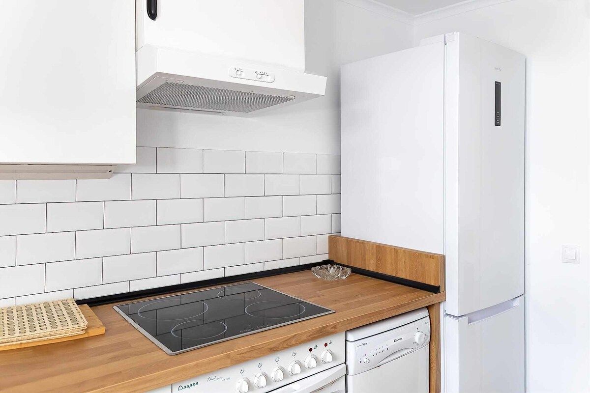 Una cocina con armarios blancos, un refrigerador blanco, una encimera de madera, una placa de inducción negra y un lavavajillas.