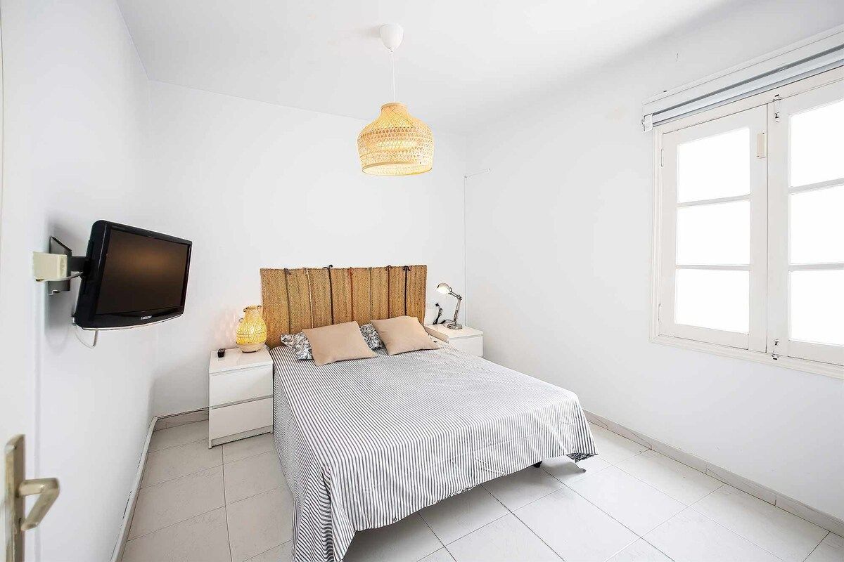 Een slaapkamer met een bed, een televisie, een bedlamp, een raam en een hangende lamp.