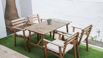 Un espace extérieur aménagé avec des meubles en bois, comprenant une table et des chaises, un pot de fleurs et un arbre.