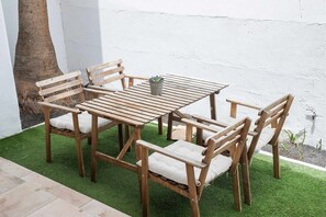 A wooden outdoor seating area with a table and chairs, a potted plant, and a tree.