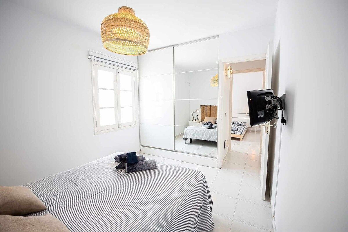 Une chambre d’hôtel équipée d’un lit, d’un grand miroir, d’une armoire et d’un téléviseur fixé au mur.