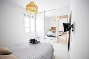 Habitación de hotel con cama, espejo grande, armario y televisor montado en la pared.