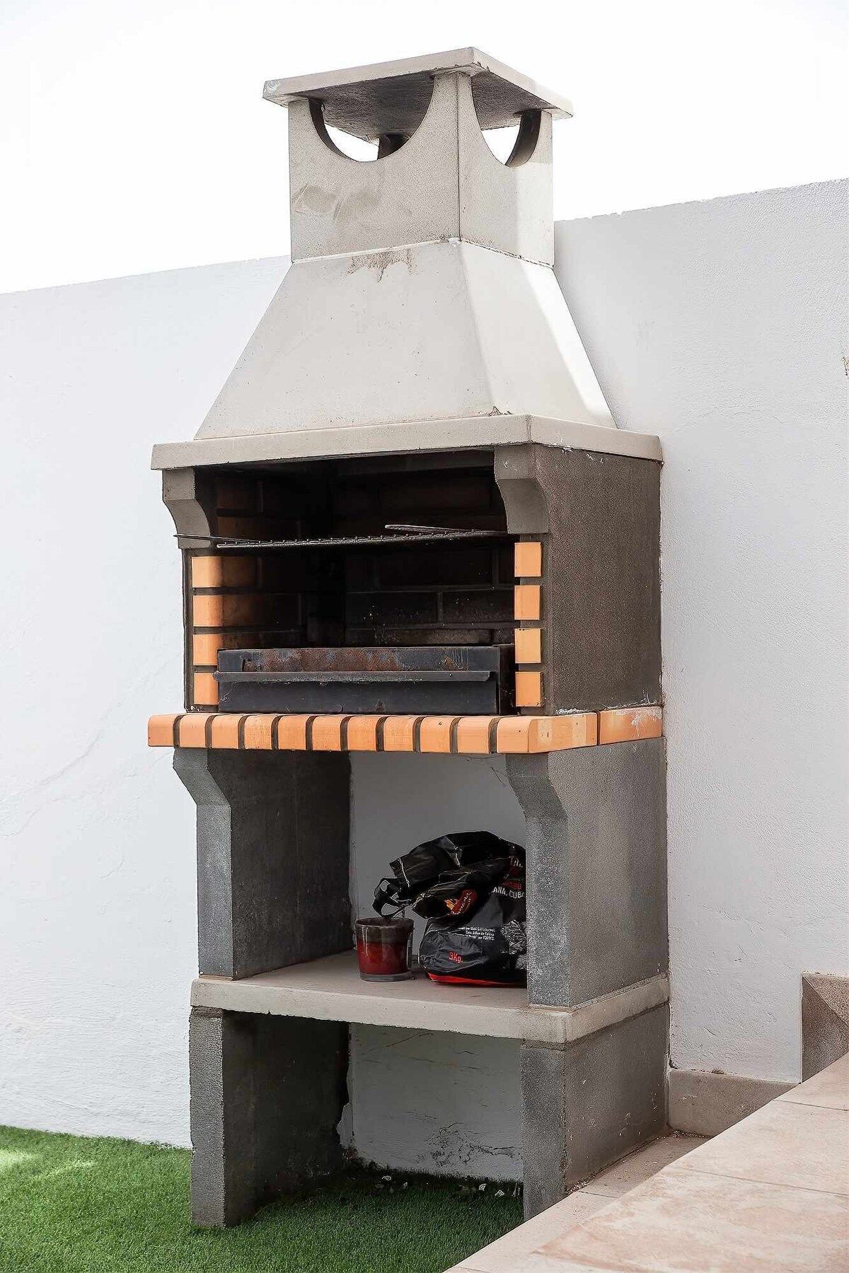 Ein Beton-Pizzaofen für den Außenbereich mit Schornstein, einer Ziegelablage und einer Tüte Holzkohle.