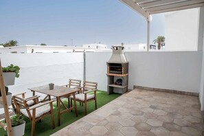 Una terraza en la azotea con una parrilla, muebles de madera y plantas en macetas.