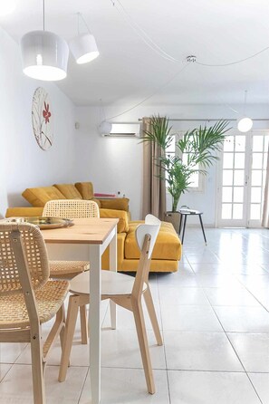 A modern living room with a dining area, featuring a sofa, chairs, a table, and a potted plant.