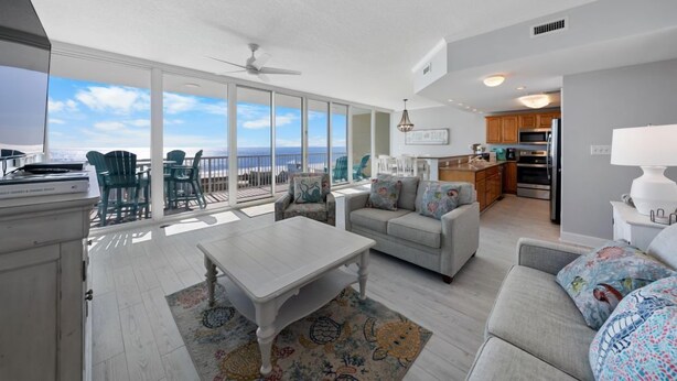 A spacious living room with a large window overlooking the ocean, a dining area, and a kitchen. - Corner Condo w/ Panoramic Views of the Gulf & Lagoon | Pool & Sauna | Sleeps 10 (Gulf Shores)