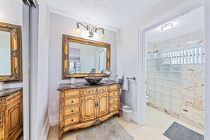 Bagno con un ampio specchio, mobile lavabo con lavandino a incasso, armadietto in legno e zona doccia con pannelli in vetro.