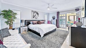 A bedroom with a bed, a nightstand, a chair, a large window, and a ceiling fan.