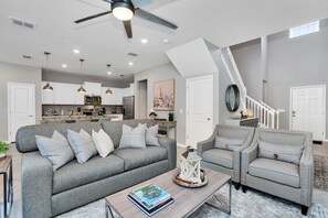 A modern living room with a grey sofa, a coffee table with books, a white armchair, and a staircase leading to an upper level.