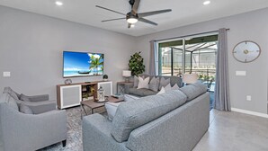 Ein modernes Wohnzimmer mit grauen Sofas, einem Flachbildfernseher und einem Deckenventilator.