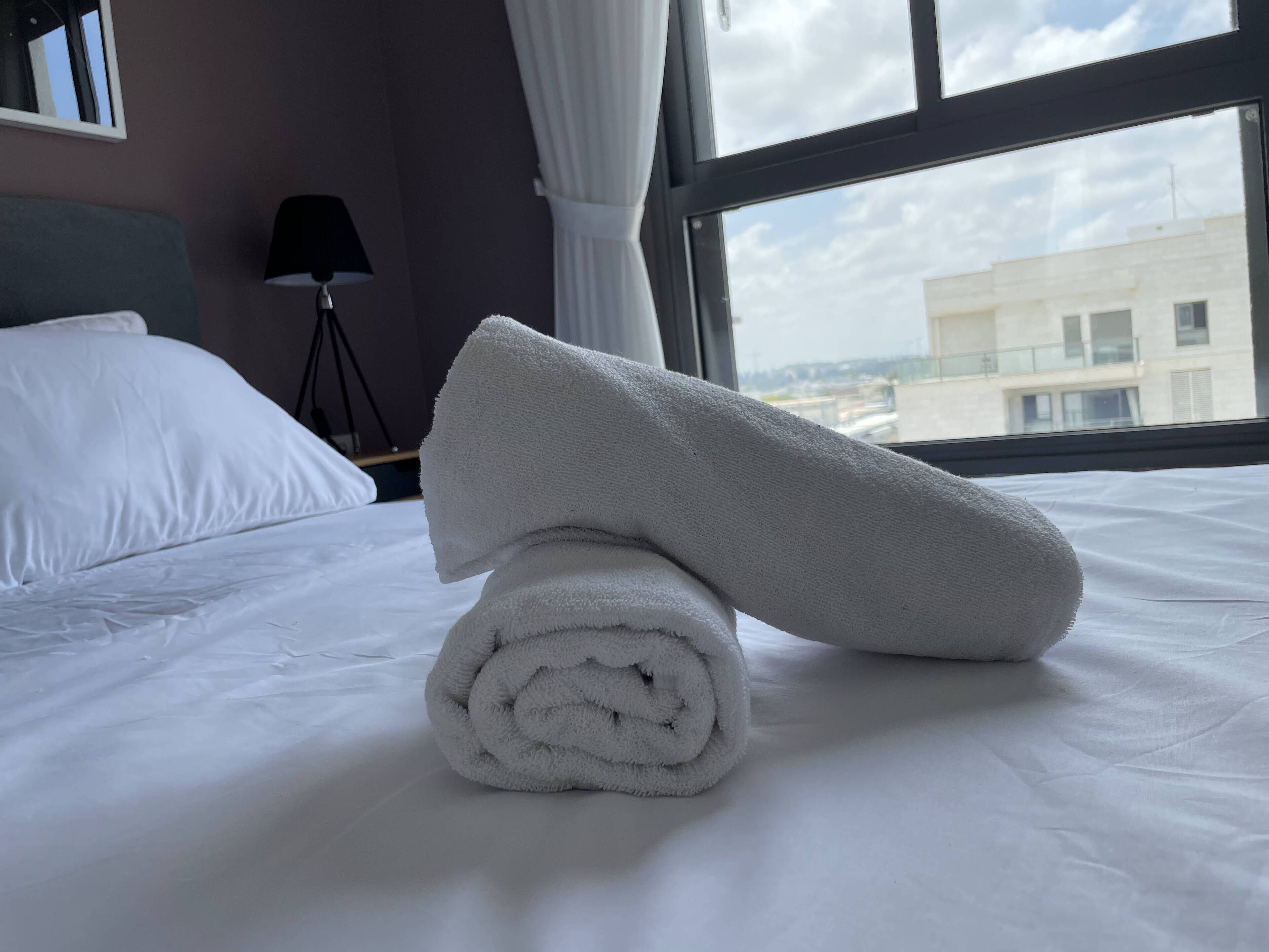 Una cama bien hecha con sábanas blancas y una toalla enrollada encima.
