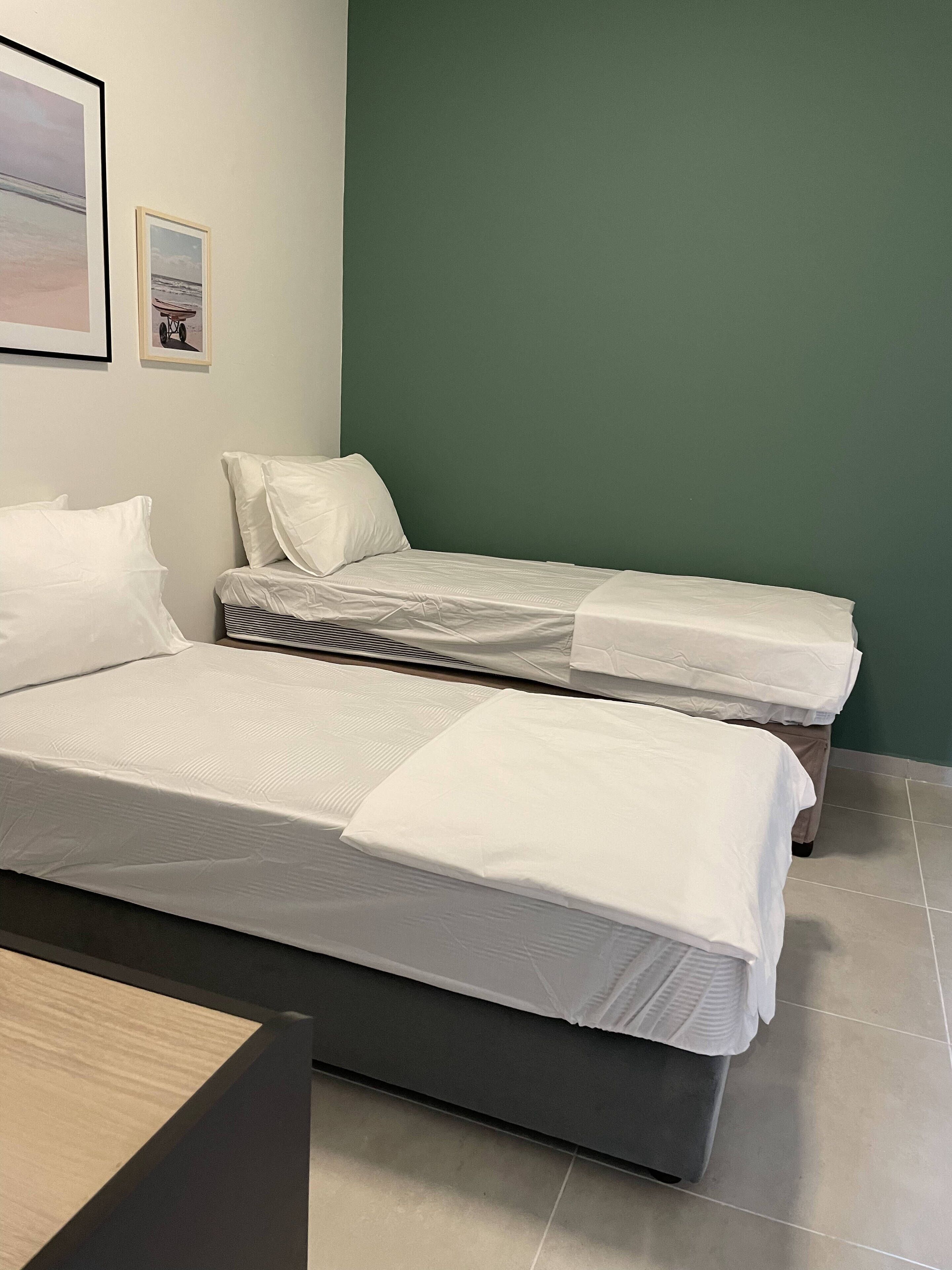 A hotel room with two single beds, a wooden desk, and a green accent wall.