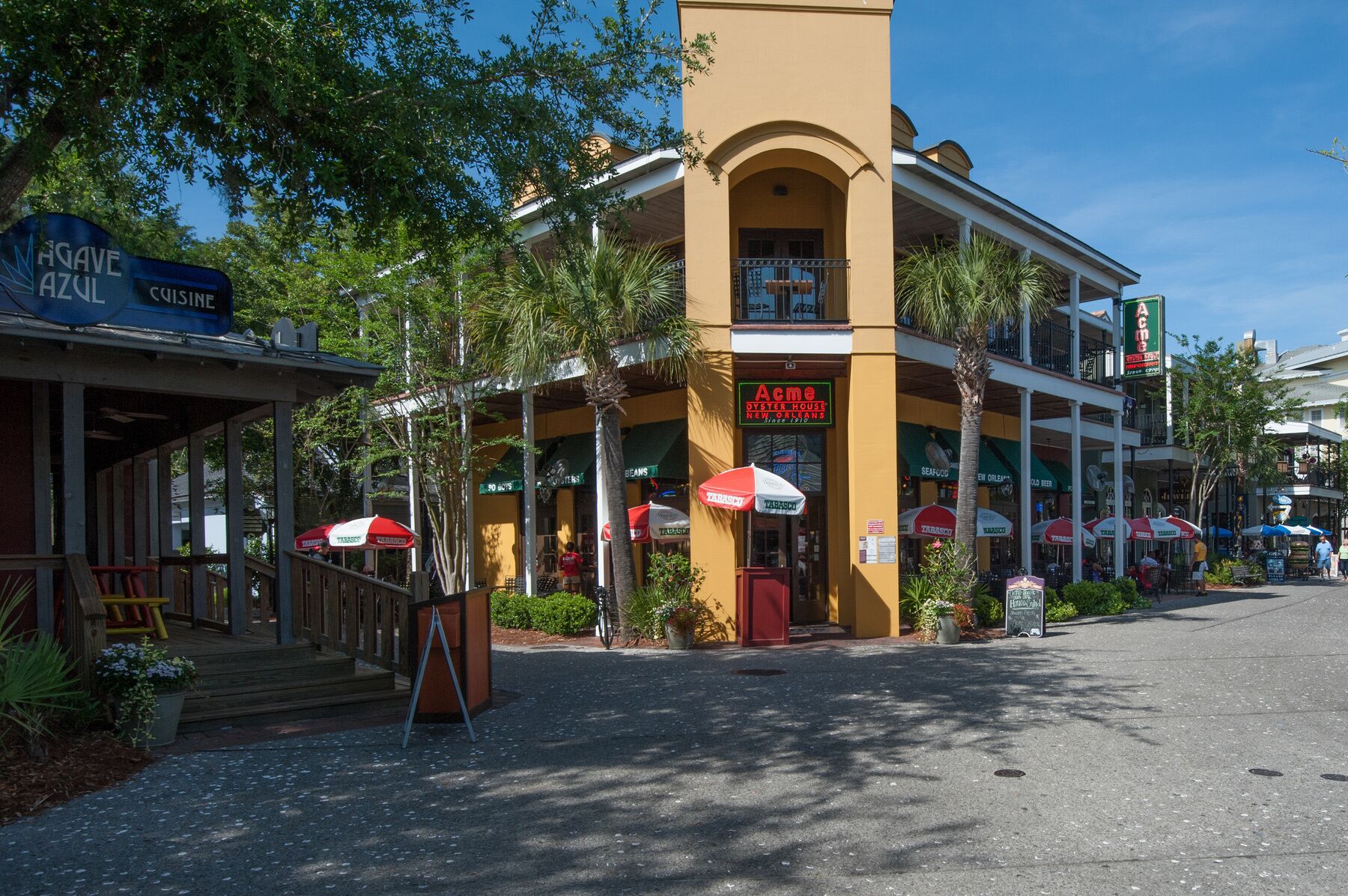 A building with a yellow facade, a sign for 'Acme Oyster House', and outdoor seating with umbrellas.