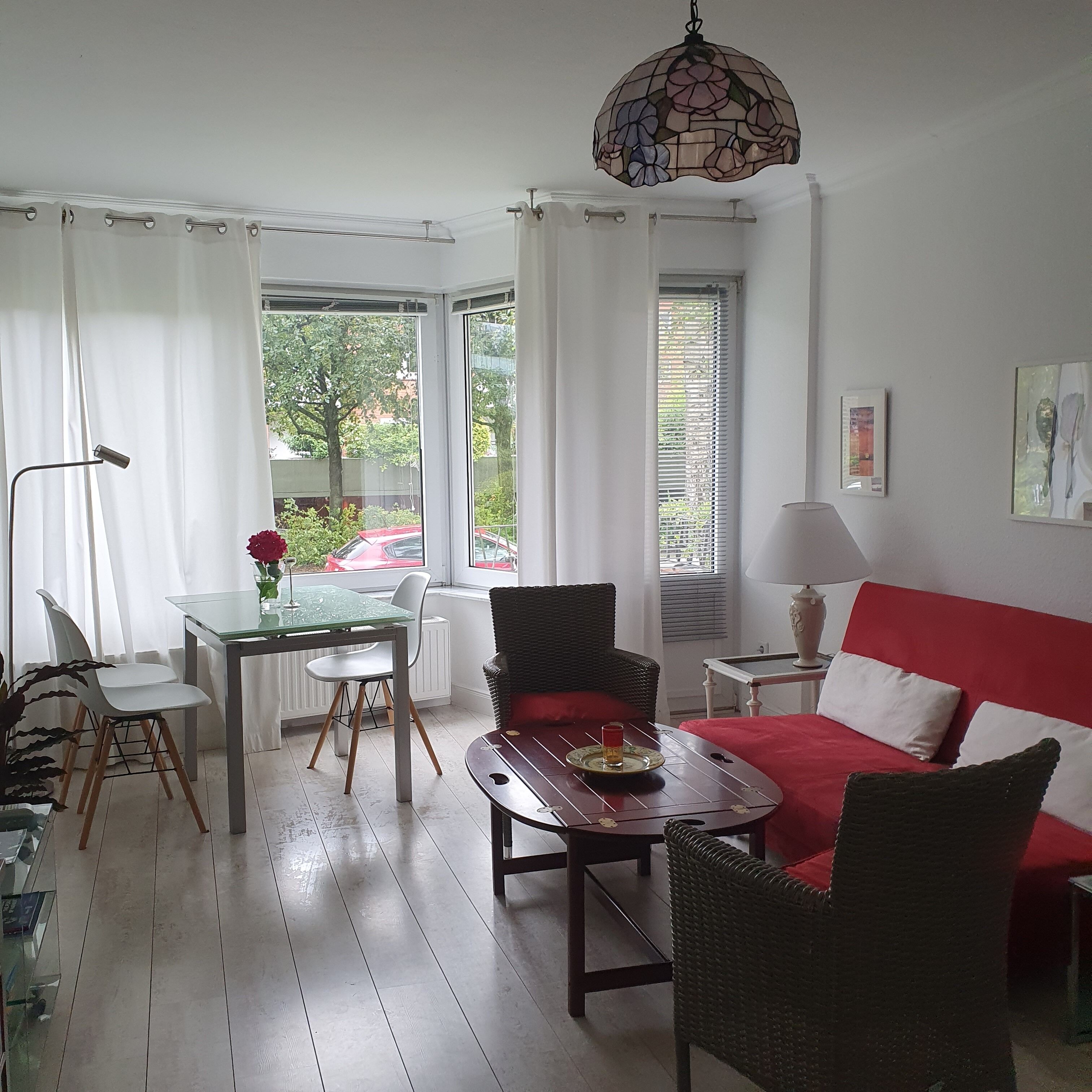 Ein gut beleuchteter Raum mit Esstisch, Stühlen, einer Couch und einer Pendelleuchte.