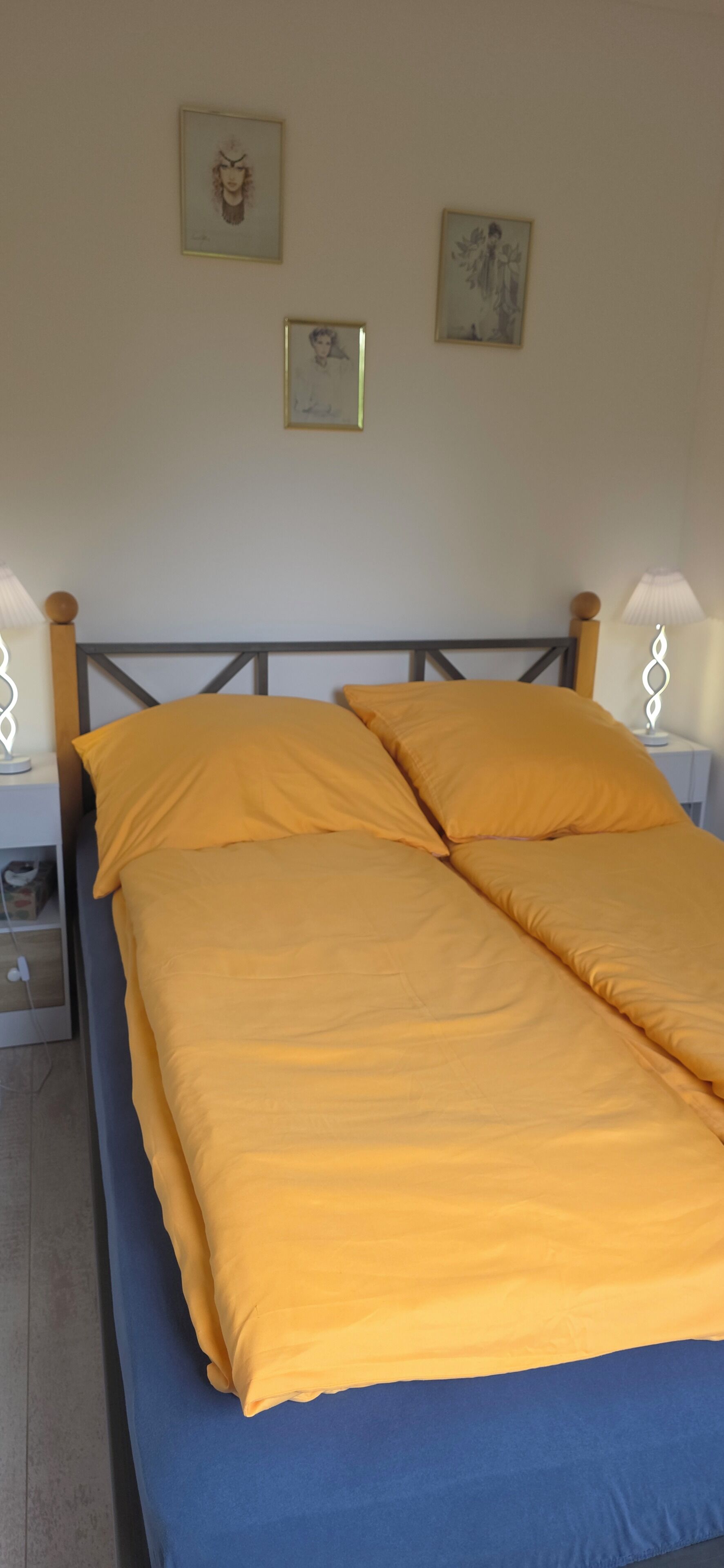 Ein Bett mit gelber Bettwäsche, einem Holz-Kopfteil und zwei Nachttischlampen.