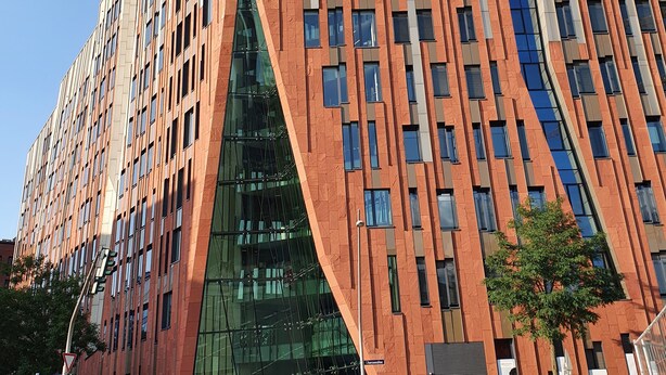 Un edificio moderno con una fachada angulosa distintiva, ventanas amplias y una entrada de vidrio destacada.