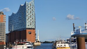 Un edificio moderno con una fachada ondulada singular, un río con barcos y un cielo azul despejado.