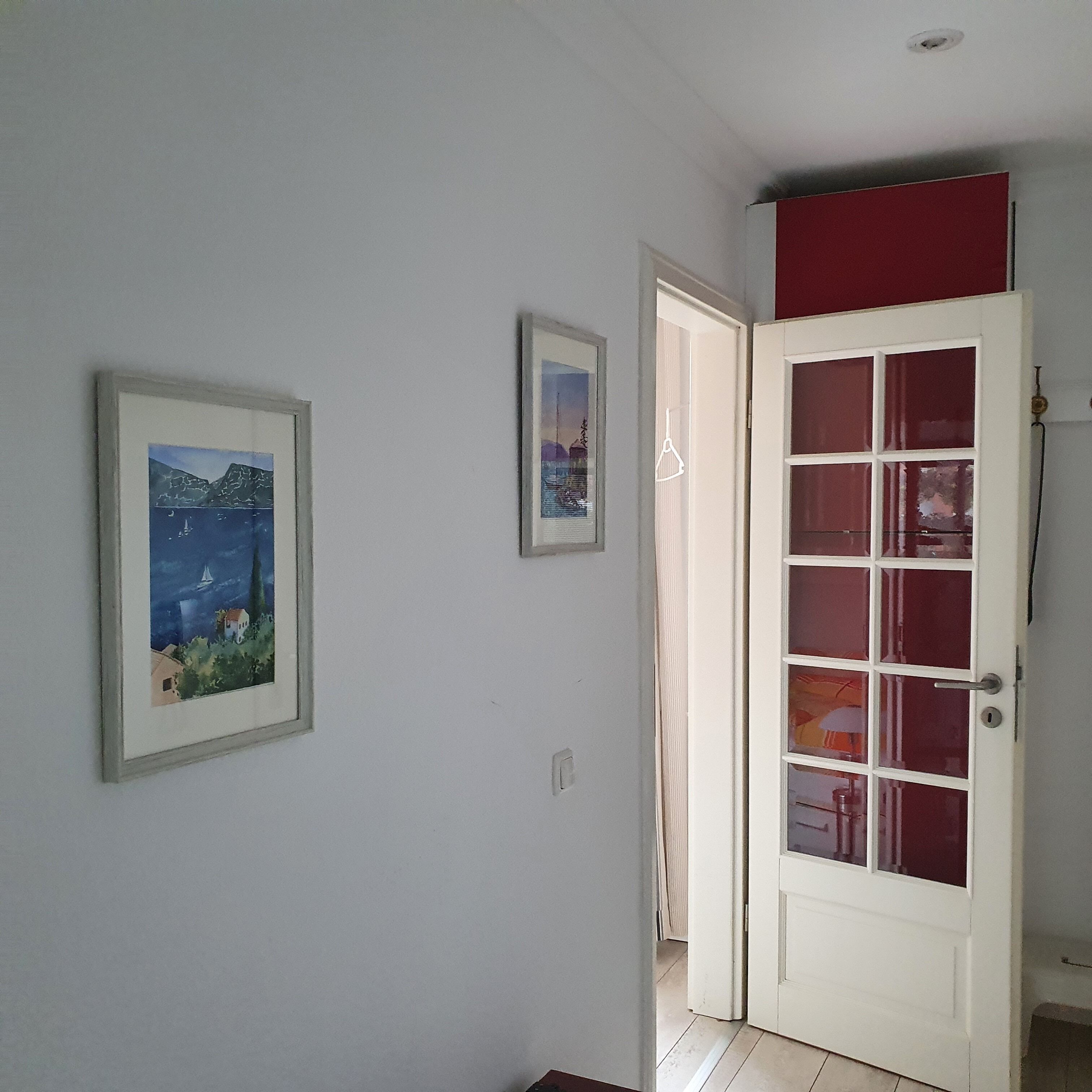 Ein Flur mit einer weißen Tür, einem gerahmten Landschaftsbild und einem kleinen Fenster.