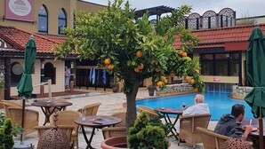 Un patio al aire libre con mobiliario de mimbre, una piscina y un naranjo.
