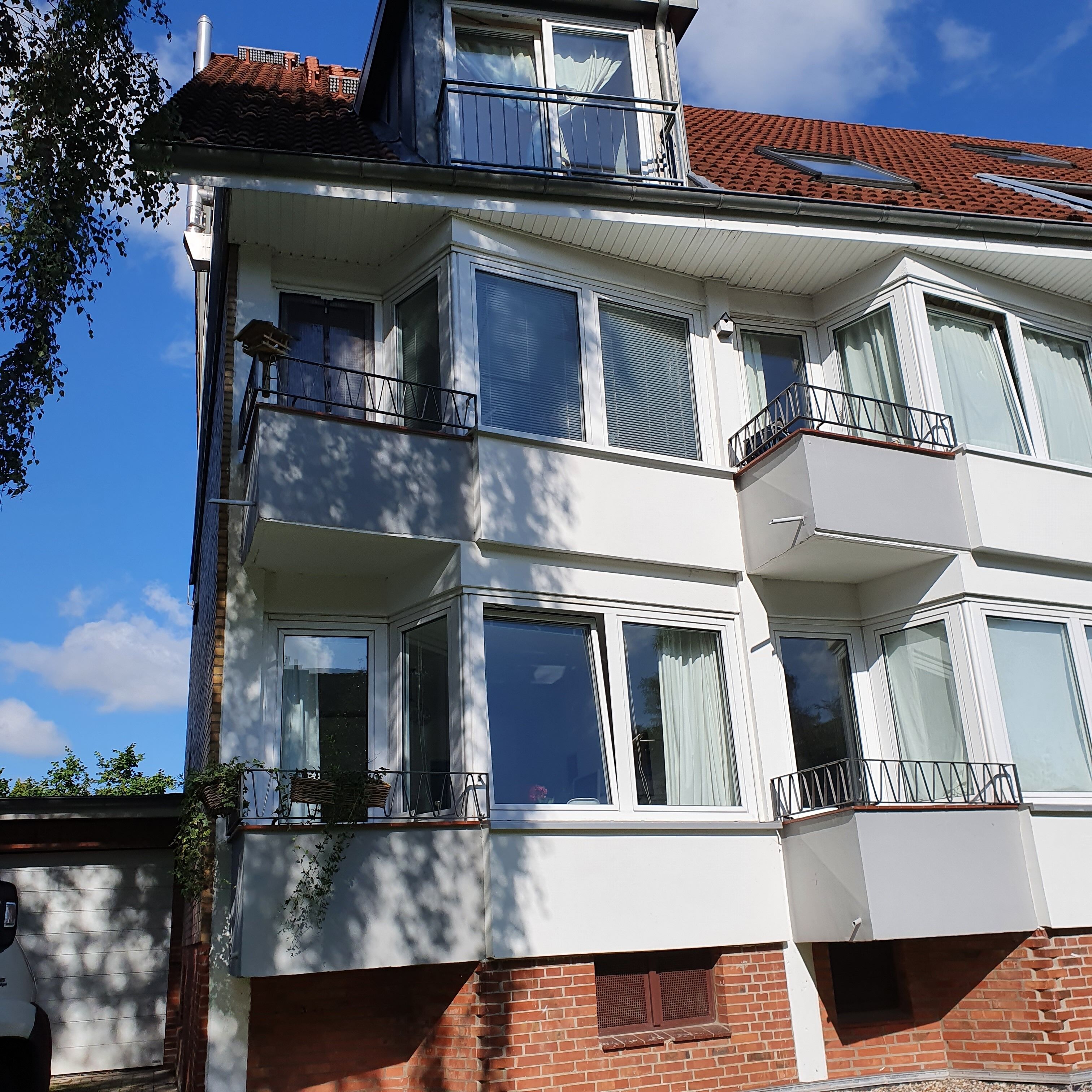 A multi-story residential building with large windows, balconies, and a red-tiled roof.