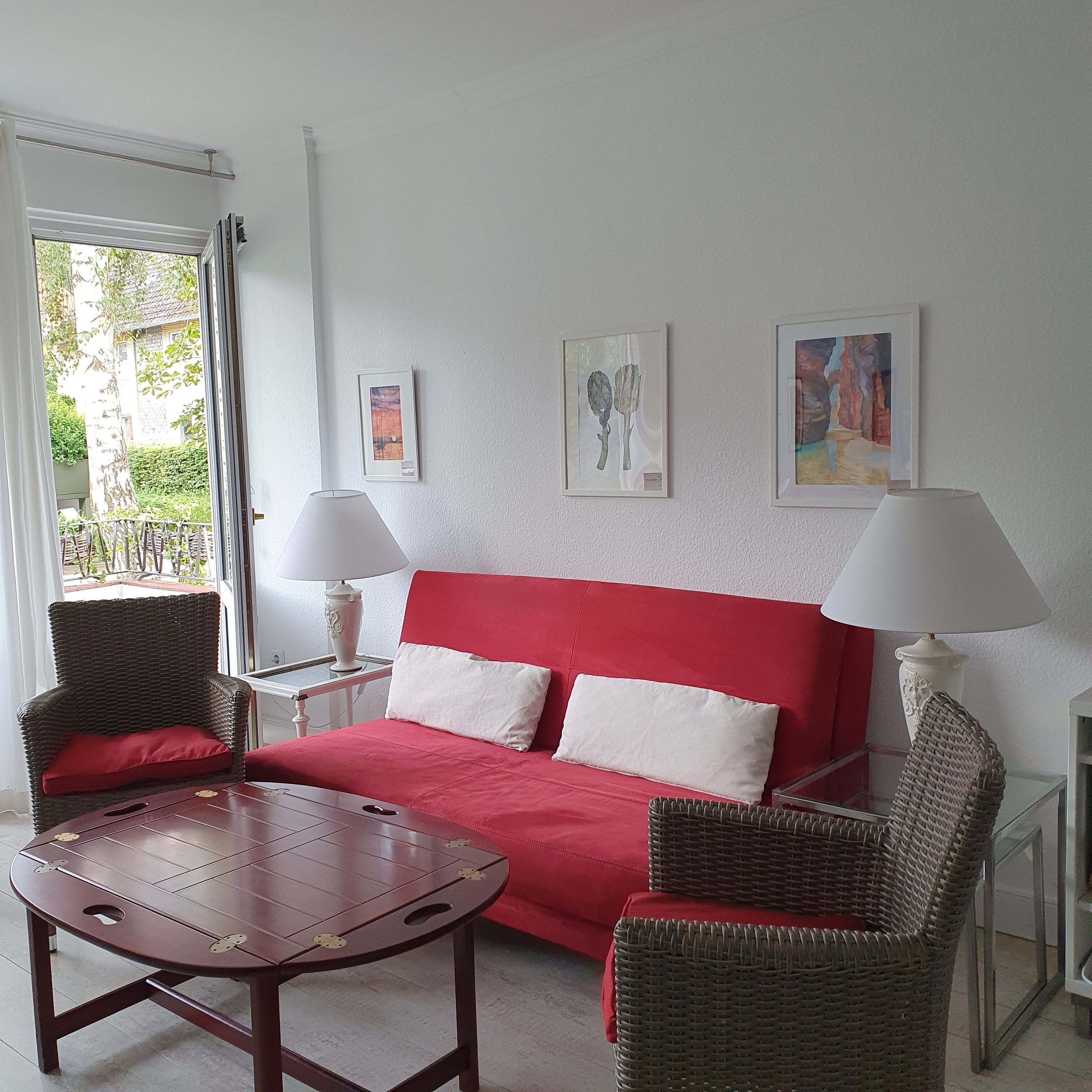 A room with a red sofa, two wicker chairs, a small wooden table, and two wall-mounted lamps.