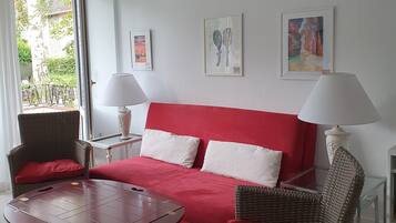 A room with a red sofa, two wicker chairs, a small wooden table, and two wall-mounted lamps.