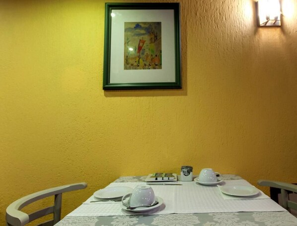 A dining table set with plates, bowls, and cups, with a framed artwork above. - Albergaria Senhora a Branca (Braga)