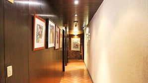Un couloir avec des tableaux encadrés accrochés au mur, un sol carrelé et un mur de briques au fond.