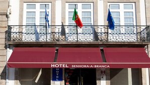 La façade d’un hôtel, ornée d’un auvent bordeaux, de drapeaux et d’une enseigne indiquant qu’il s’agit de l’HÔTEL SENHORA-A-BRANCA.